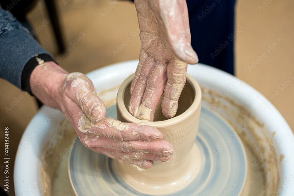The woman potter's hands formed by a clay pot on a potter's wheel. The potter works in a workshop