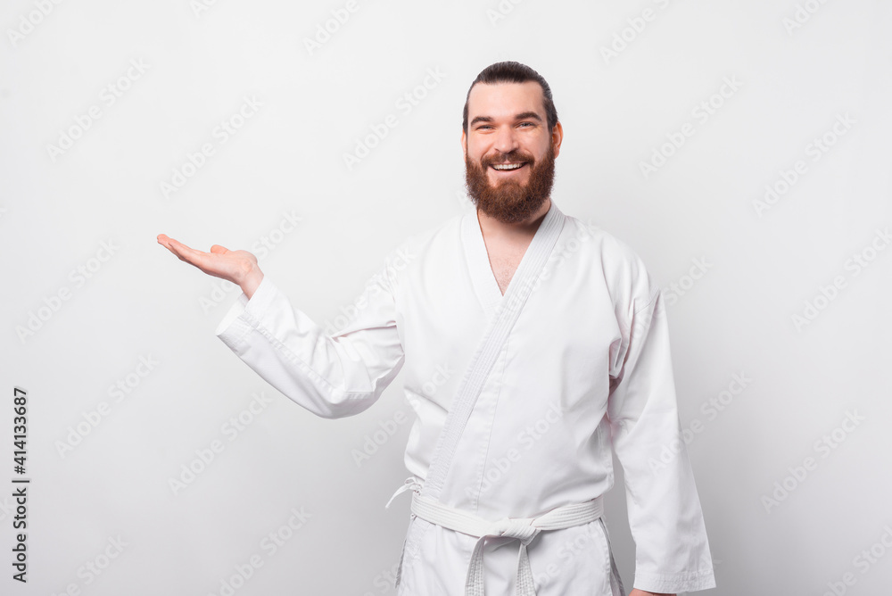 Happy bearded man in taekwondo uniform holding palm with copyspace.