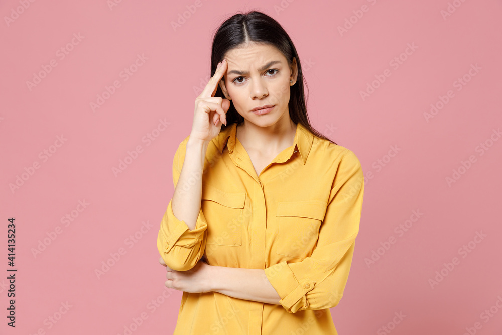 Young brunette thoughtful pensive overthinking latin student woman 20s wearing yellow casual shirt proping up forehead head looking camera isolated on pastel pink color background studio portrait. Young brunette thoughtful pensive overthinking latin student woman 20s wearing yellow casual shirt proping up forehead head looking camera isolated on pastel pink color background studio portrait.