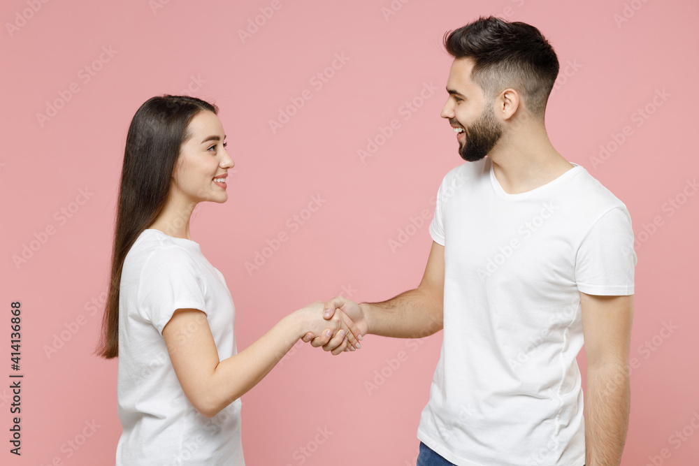 Young cheerful couple two friends man woman in white basic blank t-shirts hold hand folded handshake gesture isolated on pastel pink color background studio portrait Friendship business greet concept Young cheerful couple two friends man woman in white basic blank t-shirts hold hand folded handshake gesture isolated on pastel pink color background studio portrait Friendship business greet concept