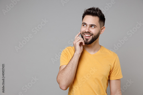 Young caucasian european dreamful bearded wistful smiling attractive man in casual yellow basic t-shirt look aside prop up chin isolated on grey background studio portrait People lifestyle concept.