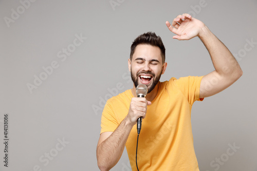 Young caucasian smiling bearded handsome student happy man 20s wear casual yellow basic t-shirt sing song in microphone enjoying leisure time dancing isolated on grey color background studio portrait. photo