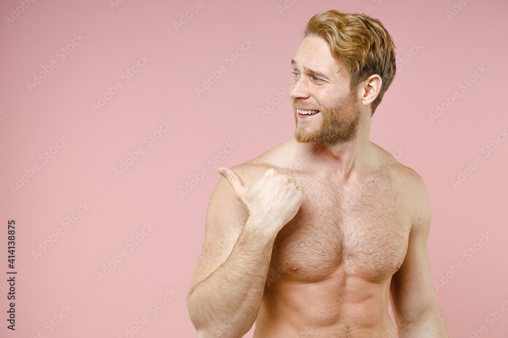 Fototapeta premium Handsome smiling bearded naked young man 20s years old perfect skin pointing thumb aside isolated on pastel pink color background studio portrait. Skin care healthcare cosmetic procedures concept.
