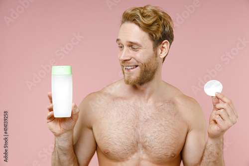 Handsome bearded naked young man 20s perfect skin hold bottle of micelar water lotion tonic cotton pad isolated on pink background studio portrait. Skin care healthcare cosmetic procedures concept. photo