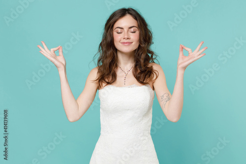 Quadro su tela Smiling tender bride woman in white wedding dress hold hands in yoga gesture relaxing meditating trying to calm down isolated on blue turquoise background studio