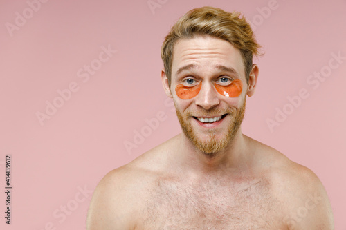 Close up of cheerful bearded naked young man 20s perfect skin wearing moisturizing patches under eyes isolated on pink background studio portrait. Skin care healthcare cosmetic procedures concept.