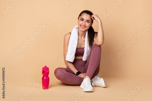 Sporty smiling woman sitting on floor with water bottle