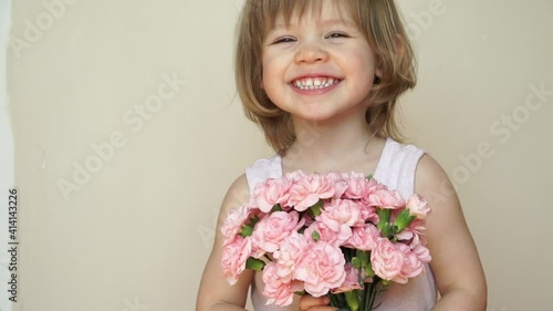 Portrait of little child girl holds bouquet of flowers, pink carnations, looks at camera, laughs, smiles and smells flowers. Spring and holiday concept