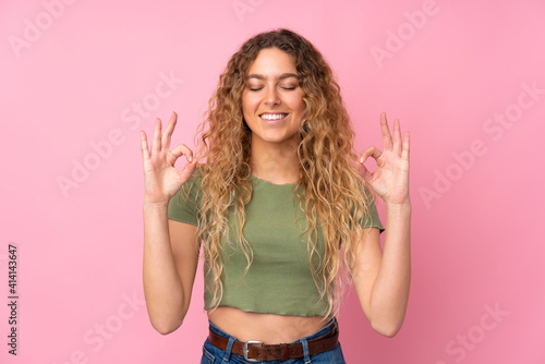 Young blonde woman with curly hair isolated on pink background in zen pose