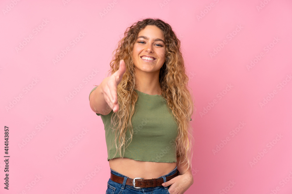 Young blonde woman with curly hair isolated on pink background shaking hands for closing a good deal Young blonde woman with curly hair isolated on pink background shaking hands for closing a good deal