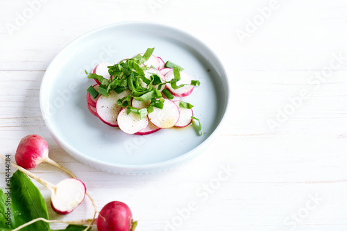 Fresh spring radish salad in blue bowl on white wooden background.Vegetarian vegetable salad.Healthy vegan food.Top view