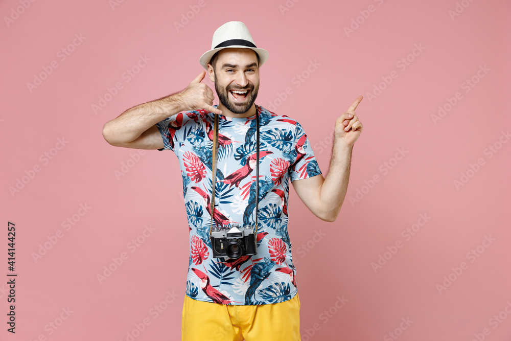 Funny young traveler tourist man in hat photo camera doing phone gesture say call me back point aside up isolated on pink background. Passenger traveling abroad on weekend. Air flight journey concept.