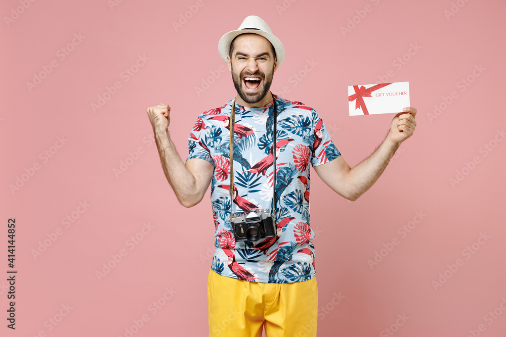 Naklejka premium Happy young traveler tourist man in summer basic clothes hat hold gift certificate doing winner gesture isolated on pink background studio. Passenger traveling on weekends. Air flight journey concept.