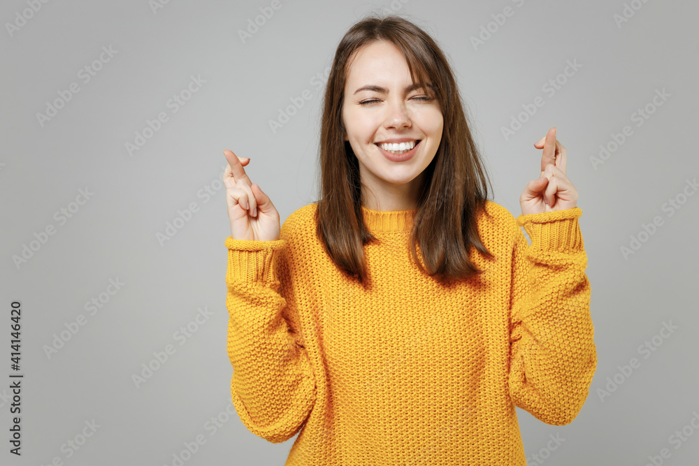 Young pretty attractive cute woman 20s wearing casual knitted yellow sweater waiting for special moment, keeping fingers crossed, making wish, eyes closed isolated on grey background studio portrait. Young pretty attractive cute woman 20s wearing casual knitted yellow sweater waiting for special moment, keeping fingers crossed, making wish, eyes closed isolated on grey background studio portrait.