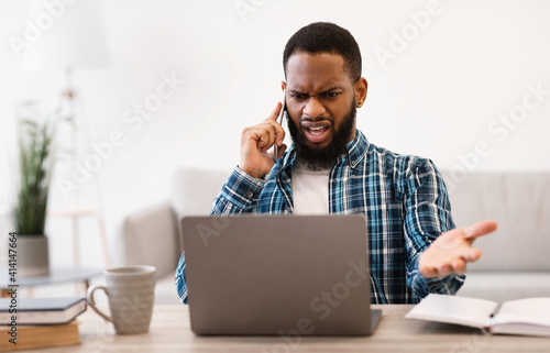 Displeased African Business Guy Talking On Phone Sitting In Office