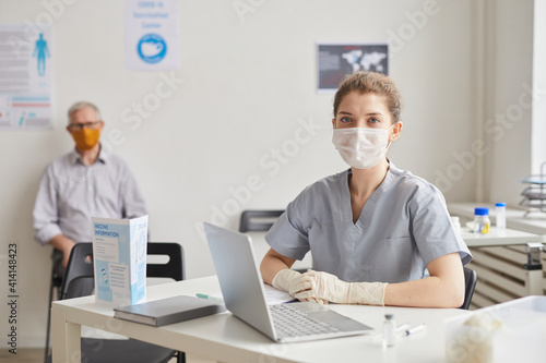 Portrait of young female doctor wearing mask and looking at camera while waiting for patients in clinic or vaccination center, copy space
