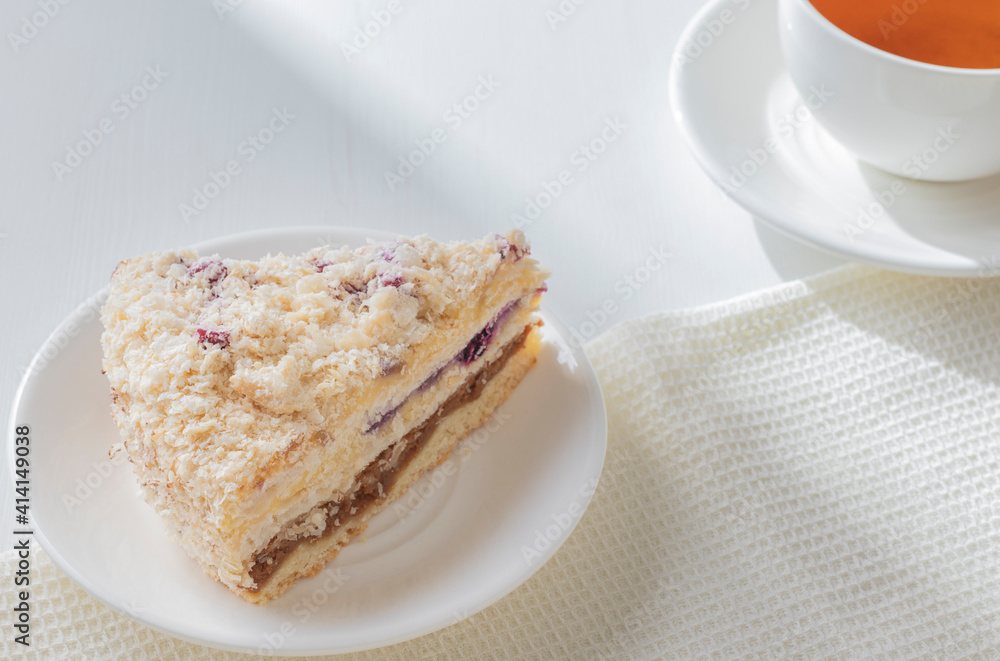 Piece of delicious napoleon cake with sour cherry on white plate with cup of tea. Direct sunlight rays on wooden table. Breakfast concept. Piece of delicious napoleon cake with sour cherry on white plate with cup of tea. Direct sunlight rays on wooden table. Breakfast concept.