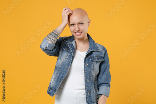 Young bald caucasian pensive thoughful troubled worried woman 20s without hair in casual jeans jacket white t-shirt look camera sctratch temple head isolated on yellow background studio portrait photo