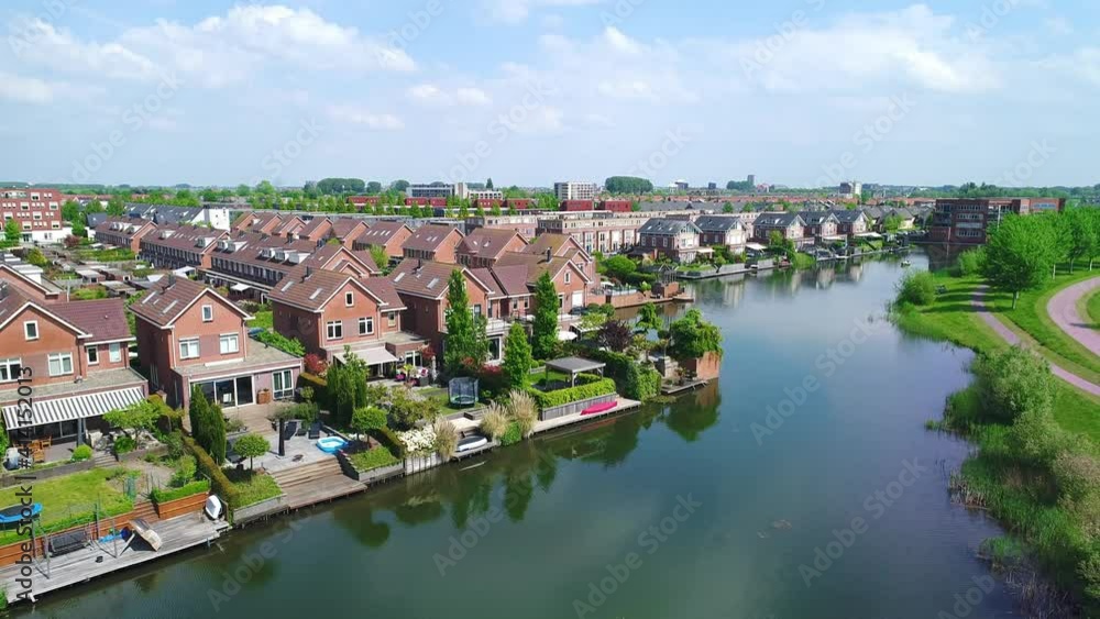 Drone flying upward over the beautiful suburb of Rotterdam in the Netherlands, the neat buildings surrounded by green trees and a river Drone flying upward over the beautiful suburb of Rotterdam in the Netherlands, the neat buildings surrounded by green trees and a river