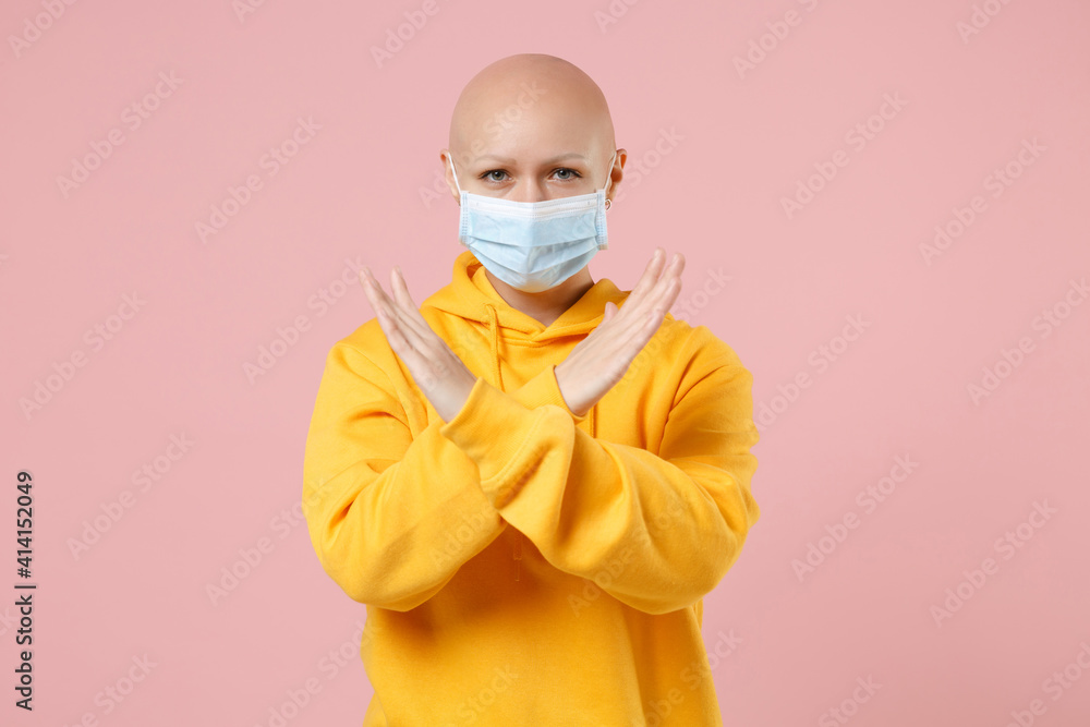 Young bald serious strict woman 20s without hair in yellow casual shirt in sterile face mask to safe coronavirus covid-19 quarantine do stop gesture crossed hands refusing isolated on pink background Young bald serious strict woman 20s without hair in yellow casual shirt in sterile face mask to safe coronavirus covid-19 quarantine do stop gesture crossed hands refusing isolated on pink background