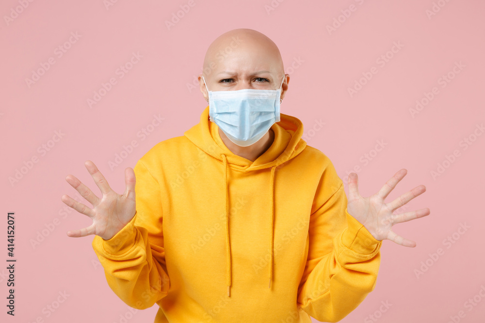 Young bald angry indignant woman 20s without hair wear yellow casual shirt in sterile face mask to safe from coronavirus virus covid-19, pandemic quarantine spread hands isolated on pink background Young bald angry indignant woman 20s without hair wear yellow casual shirt in sterile face mask to safe from coronavirus virus covid-19, pandemic quarantine spread hands isolated on pink background