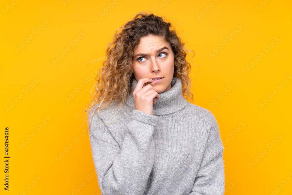 Young blonde woman with curly hair wearing a turtleneck sweater isolated on yellow background nervous and scared Young blonde woman with curly hair wearing a turtleneck sweater isolated on yellow background nervous and scared