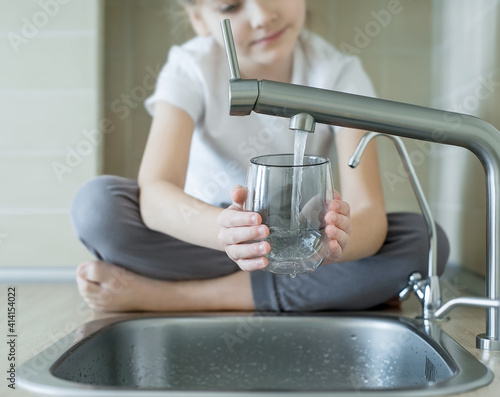 Little girl drinking from water tap or faucet in kitchen. Pouring fresh drink. Healthy lifestyle. Water quality check concept. World water monitoring day. Environmental  pollution problem
