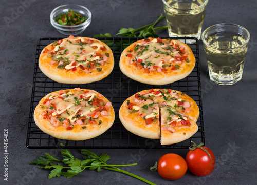 Italian mini pizzas with sausage, pickles, tomatoes, mozzarella, parsley, greens on a metal stand on a dark gray background