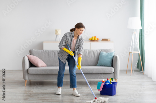 Full length portrait of happy young woman wiping floor in living room, copy space