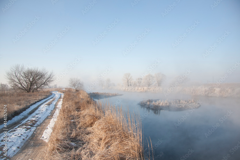 Spring landscape with a river covered with fog, melting snow on the river bank, trees