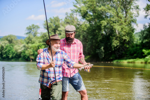 Rod tackle. Fishing equipment. Grandpa and mature man friends. Fishing with spinning reel. Sunny summer day at river. Fisherman family. Hobby sport. Fishing peaceful activity. Father and son fishing