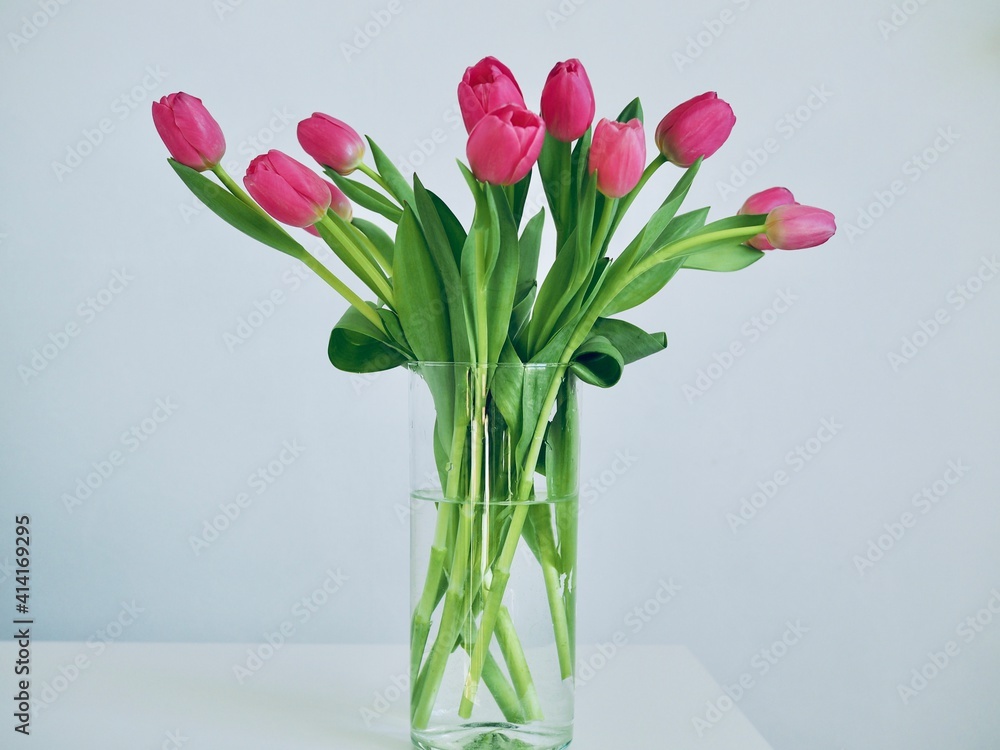 Bouquet pink tulips in glass vase stands on table on gray background. Easter day, March 8, women's day, birthday, gift, flowers for woman. Easter and spring greeting card Floristry Florist Bouquet pink tulips in glass vase stands on table on gray background. Easter day, March 8, women's day, birthday, gift, flowers for woman. Easter and spring greeting card Floristry Florist