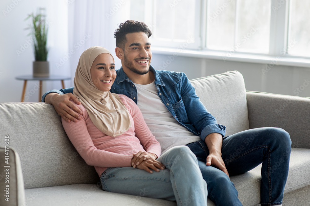Cheerful muslim couple sitting on couch at home, copy space Cheerful muslim couple sitting on couch at home, copy space