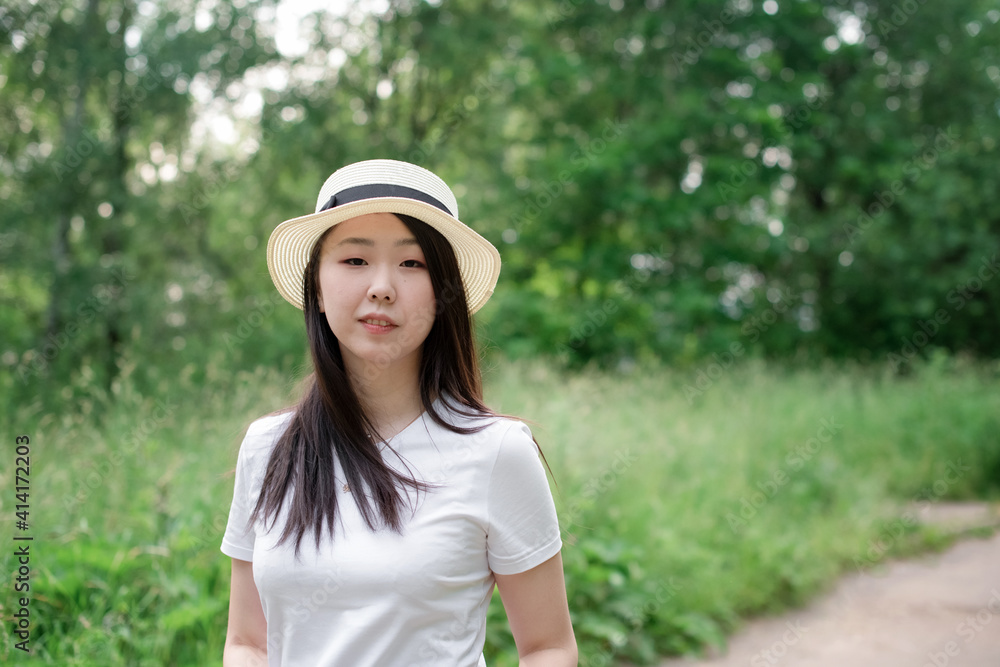 Portrait of a beautiful fashionable Asian girl in a hat in the nature of summer outdoor background.