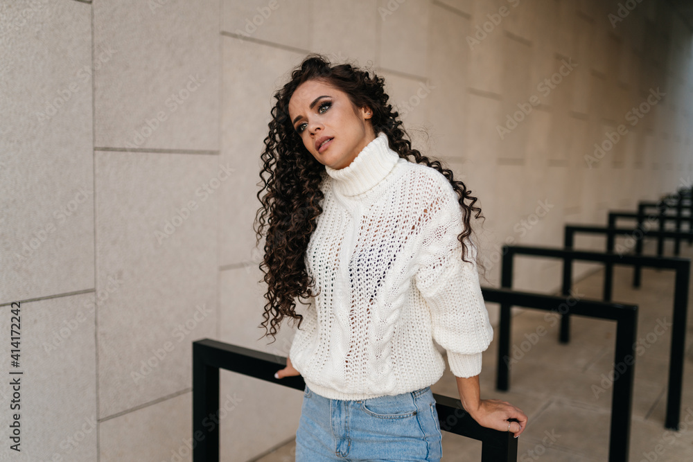 Fototapeta premium leaning behind her hands the black-haired curly-haired beauty with an attentive look looks tilting her head to the shoulder. High quality photo