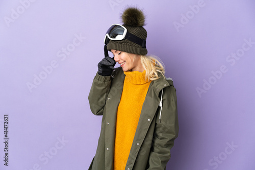 Skier Russian girl with snowboarding glasses isolated on purple background laughing