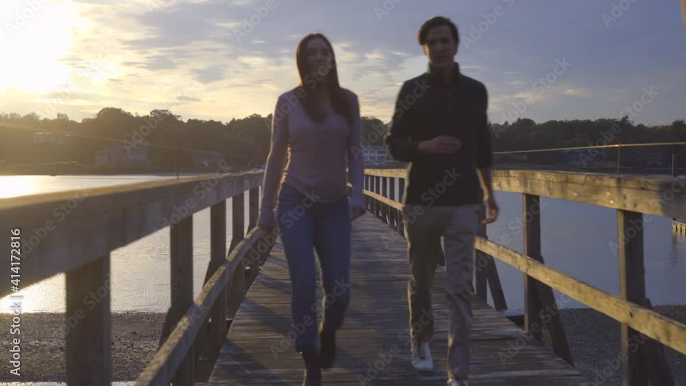 Young Man and Woman Couple Walking on Pier at Sunset Young Man and Woman Couple Walking on Pier at Sunset