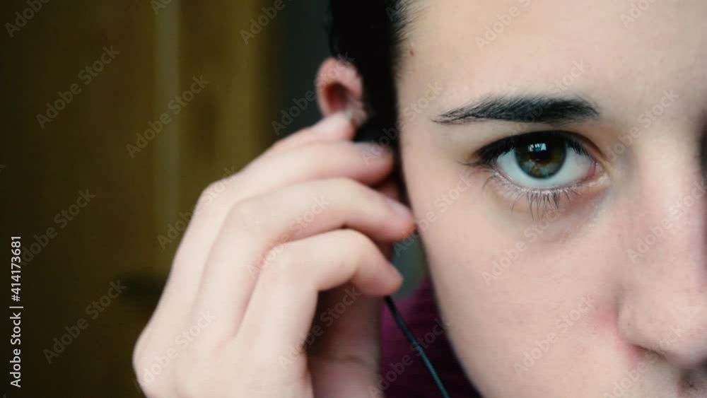 Detalle de una mujer joven poniéndose unos auriculares para escuchar música. Se ve medio rostro, ojos verdes.
