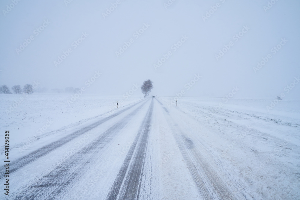 Schneebedeckte Straße bei Schneesturm im Winter mit Baum