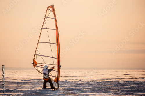 Winter windsurfing. Man riding a surf in the snow at sunset. Extreme winter sport. The rear view