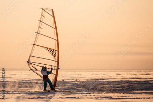 Winter windsurfing. Young woman riding a surf in the snow at sunset. Extreme winter sport. The rear view