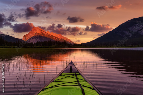 Kayaking in a beautiful lake surrounded by the Canadian Mountain Landscape. Colorful Sunset Sky Art Render. Vermilion Lakes, Banff, Alberta, Canada.