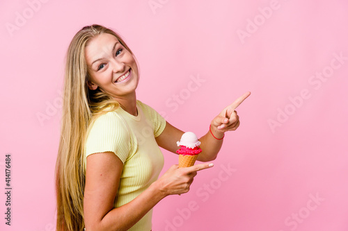 Young russian woman eating an ice cream isolated excited pointing with forefingers away.