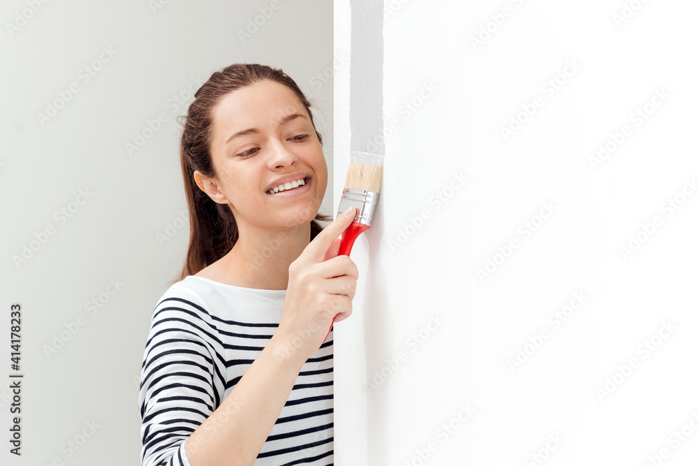 Young woman is painting the wall with paint brush Young woman is painting the wall with paint brush