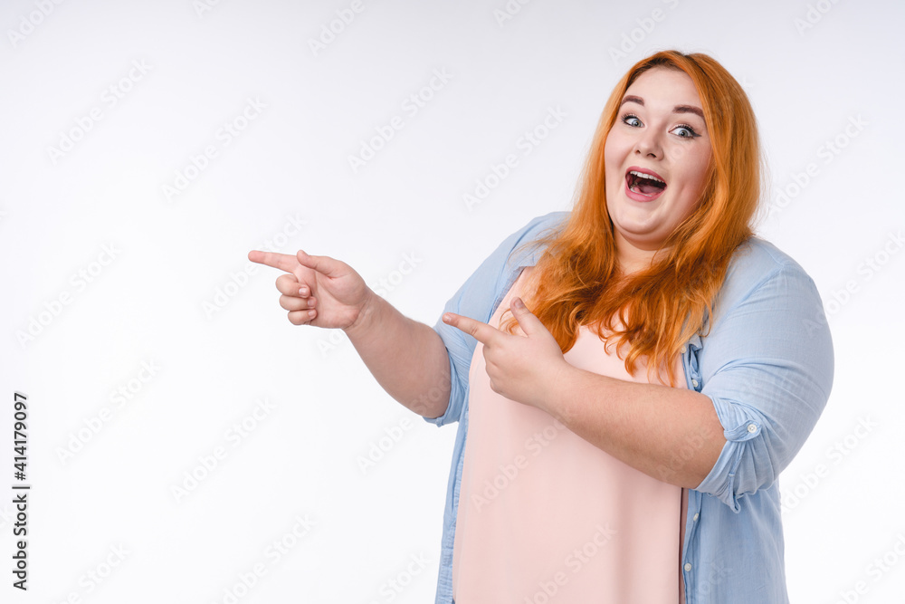 Excited young plump woman pointing at copy space isolated in white Excited young plump woman pointing at copy space isolated in white