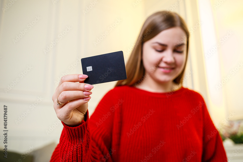 Young beautiful woman in a red sweater holding a bank card. Credit card for online purchases. Selective focus Young beautiful woman in a red sweater holding a bank card. Credit card for online purchases. Selective focus