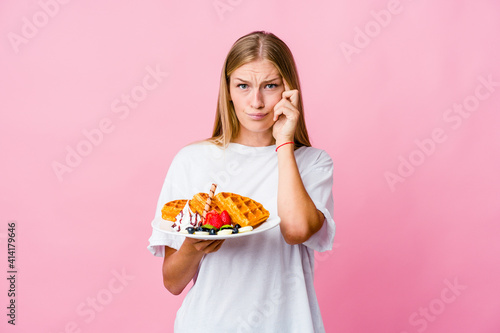Young russian woman eating a waffle isolated focused on a task, keeping forefingers pointing head.