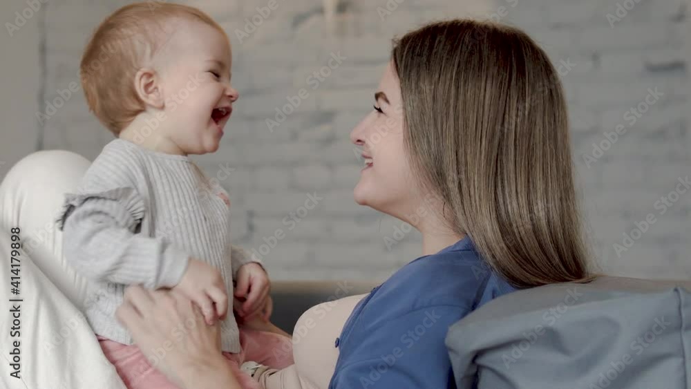 Careful mother tickling her little baby girl telling funny stories, top view Careful mother tickling her little baby girl telling funny stories, top view