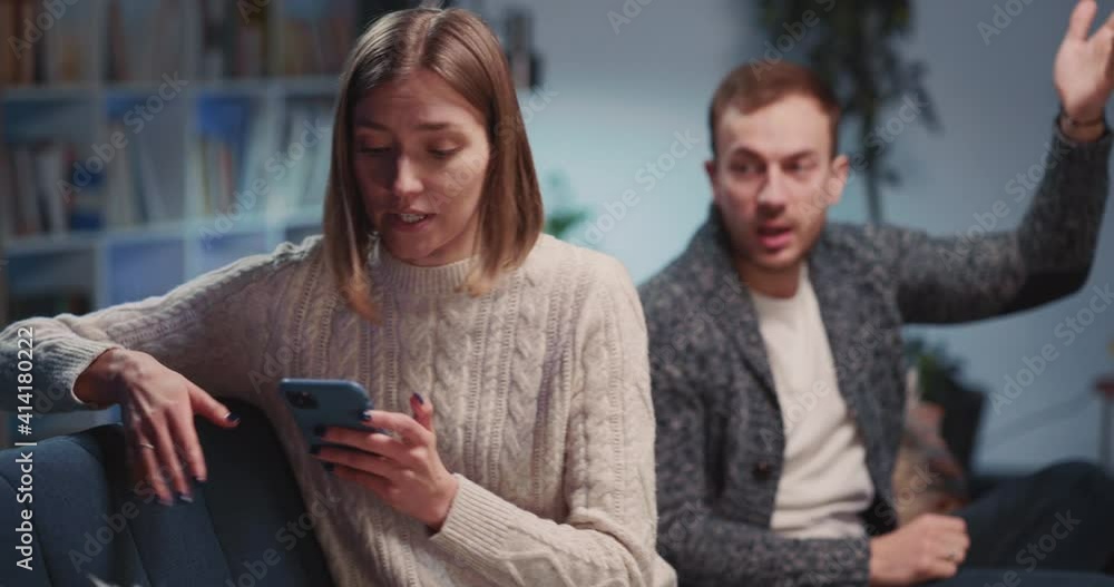 Angry caucasian sad young man and woman making up quarrel in their apartment. Emotional negative couple agruing and using mobile phones separately. Angry caucasian sad young man and woman making up quarrel in their apartment. Emotional negative couple agruing and using mobile phones separately.