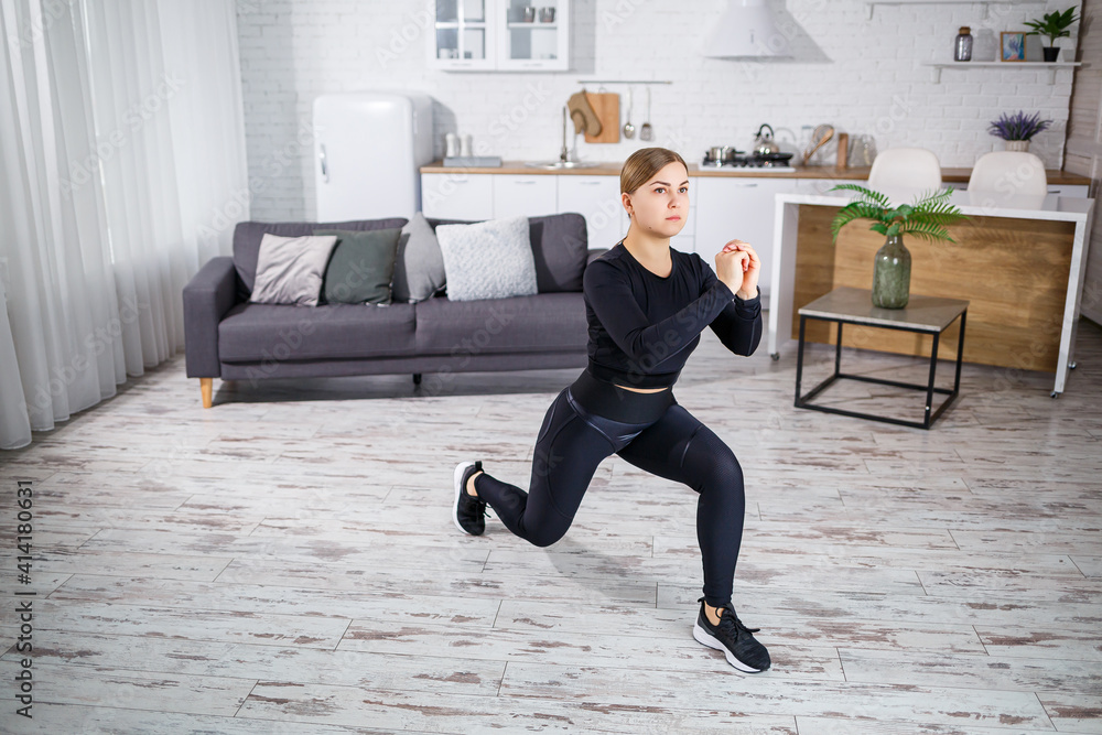 Obraz premium A young slender girl goes in for sports at home, she is dressed in fitness clothes, a black top and leggings. Fitness at home for a beautiful body